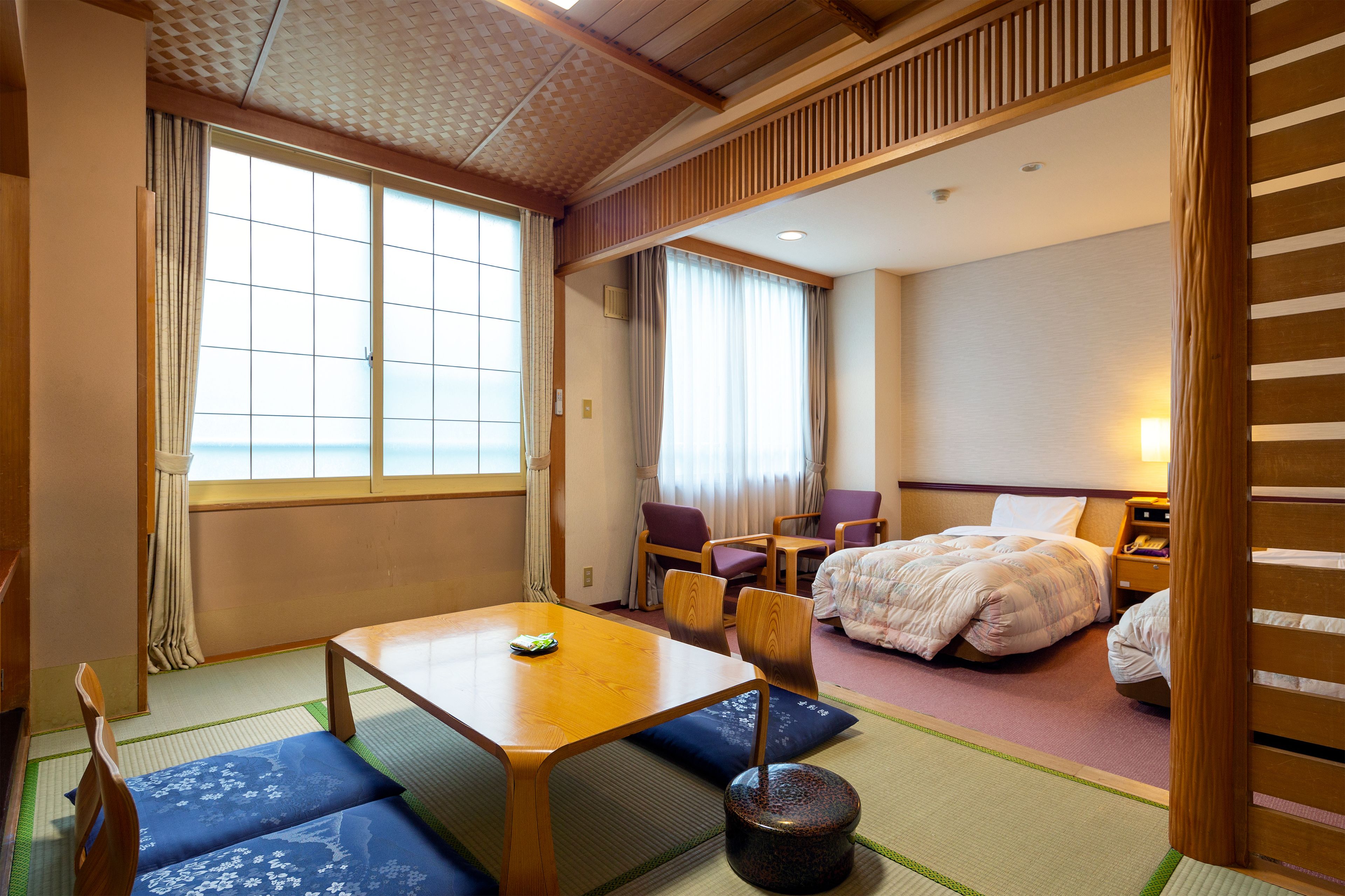 A traditional Japanese room with tatami flooring, a low table, and a bed with a white comforter.