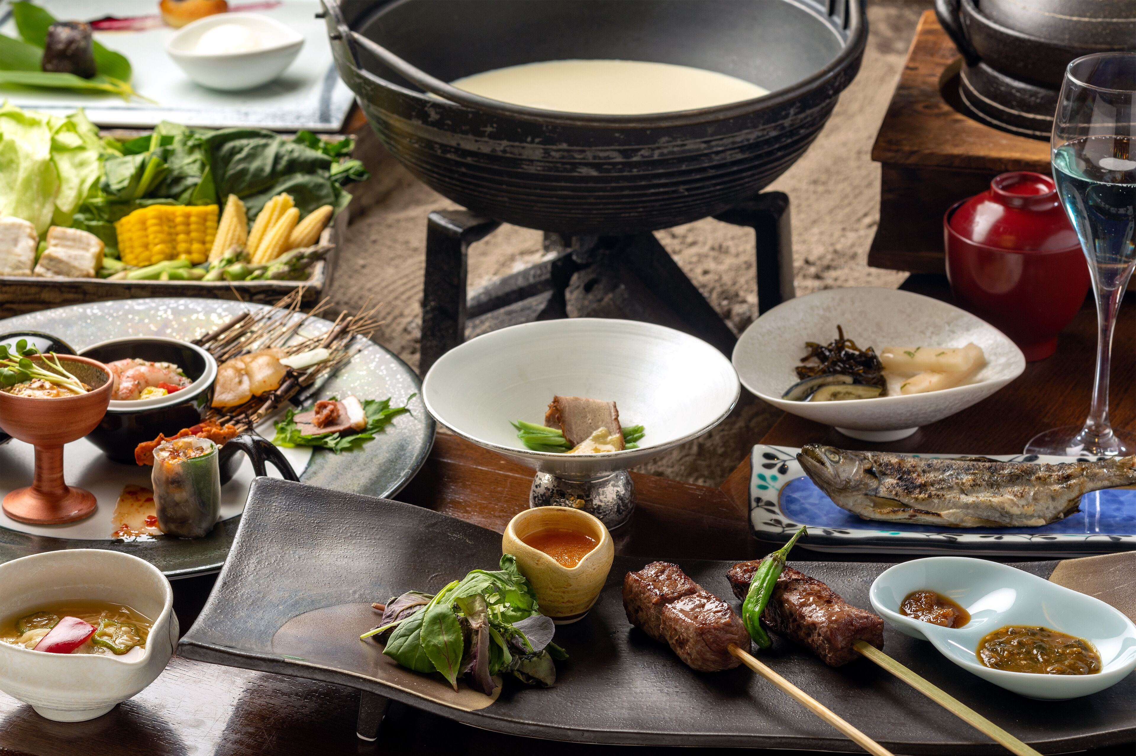 A variety of dishes including grilled fish, skewers, and vegetables, served on a wooden table.