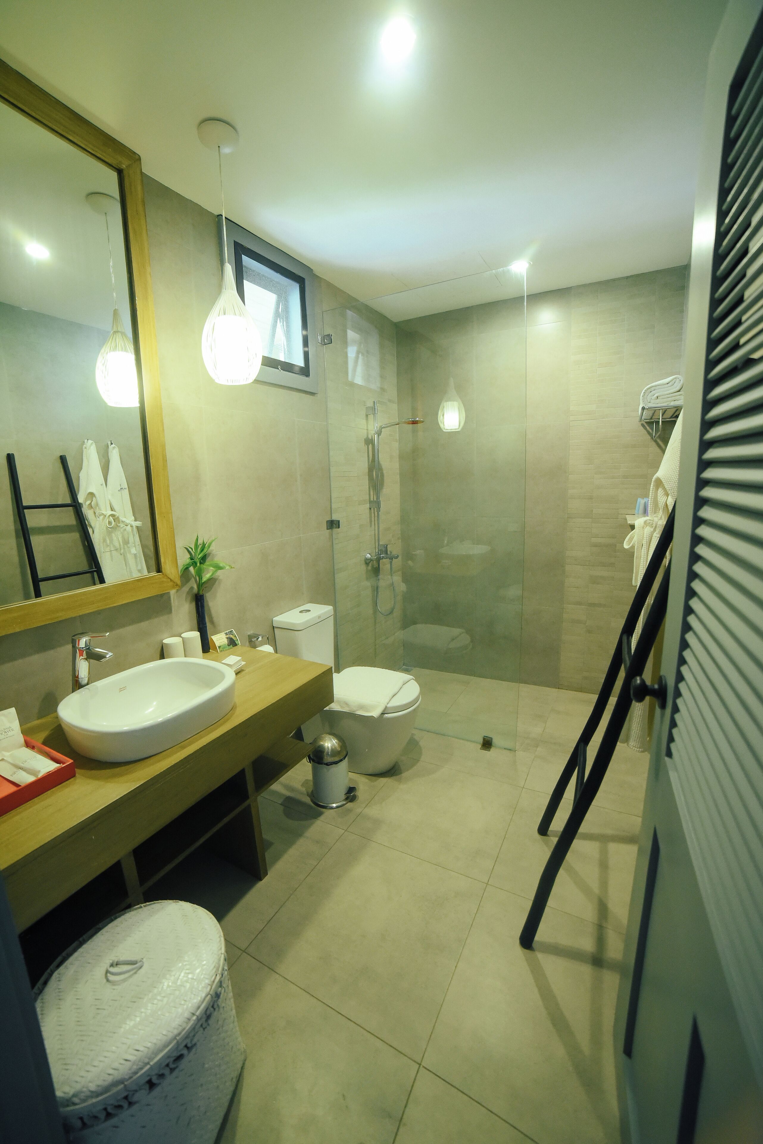 Un baño moderno con un espejo grande, un tocador de madera, un lavabo blanco, un inodoro y una ducha con mampara de vidrio.