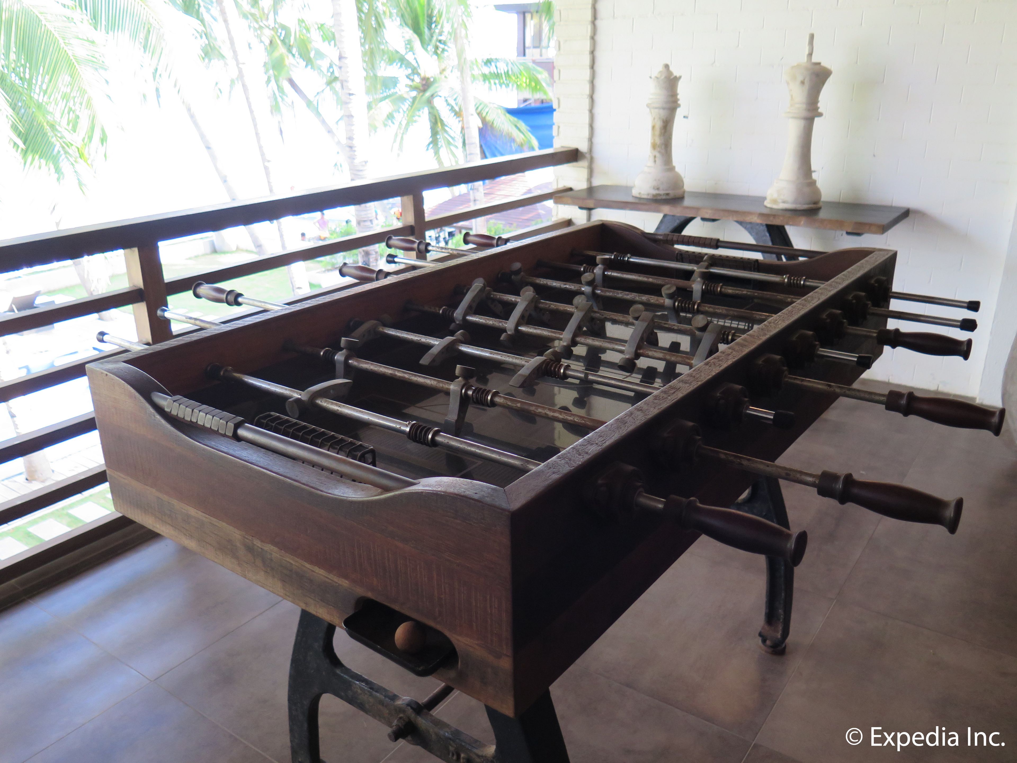 A wooden foosball table with metal rods and handles, set against a white wall with two white statues.