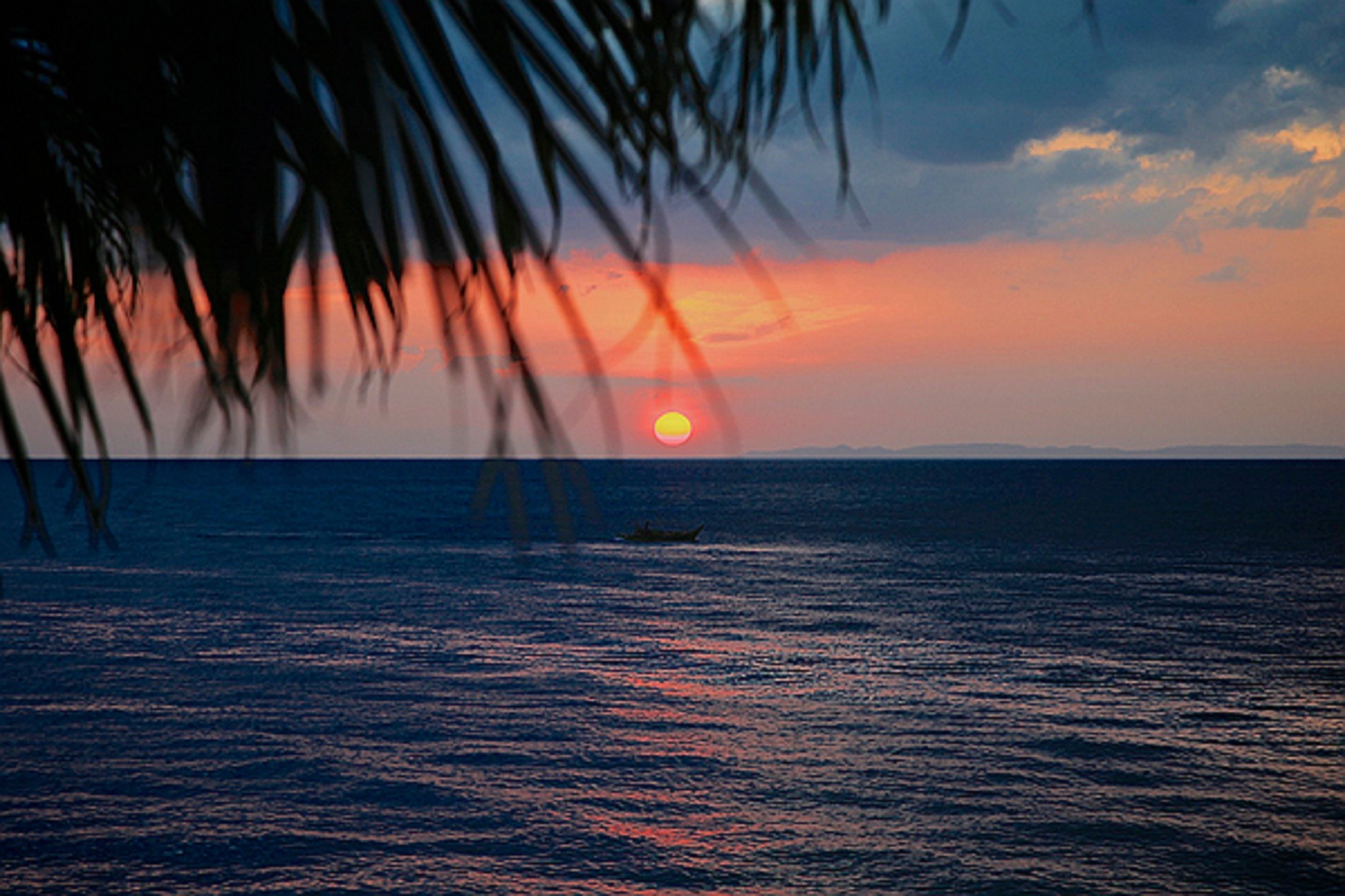 A sunset over a calm sea with a boat in the distance.