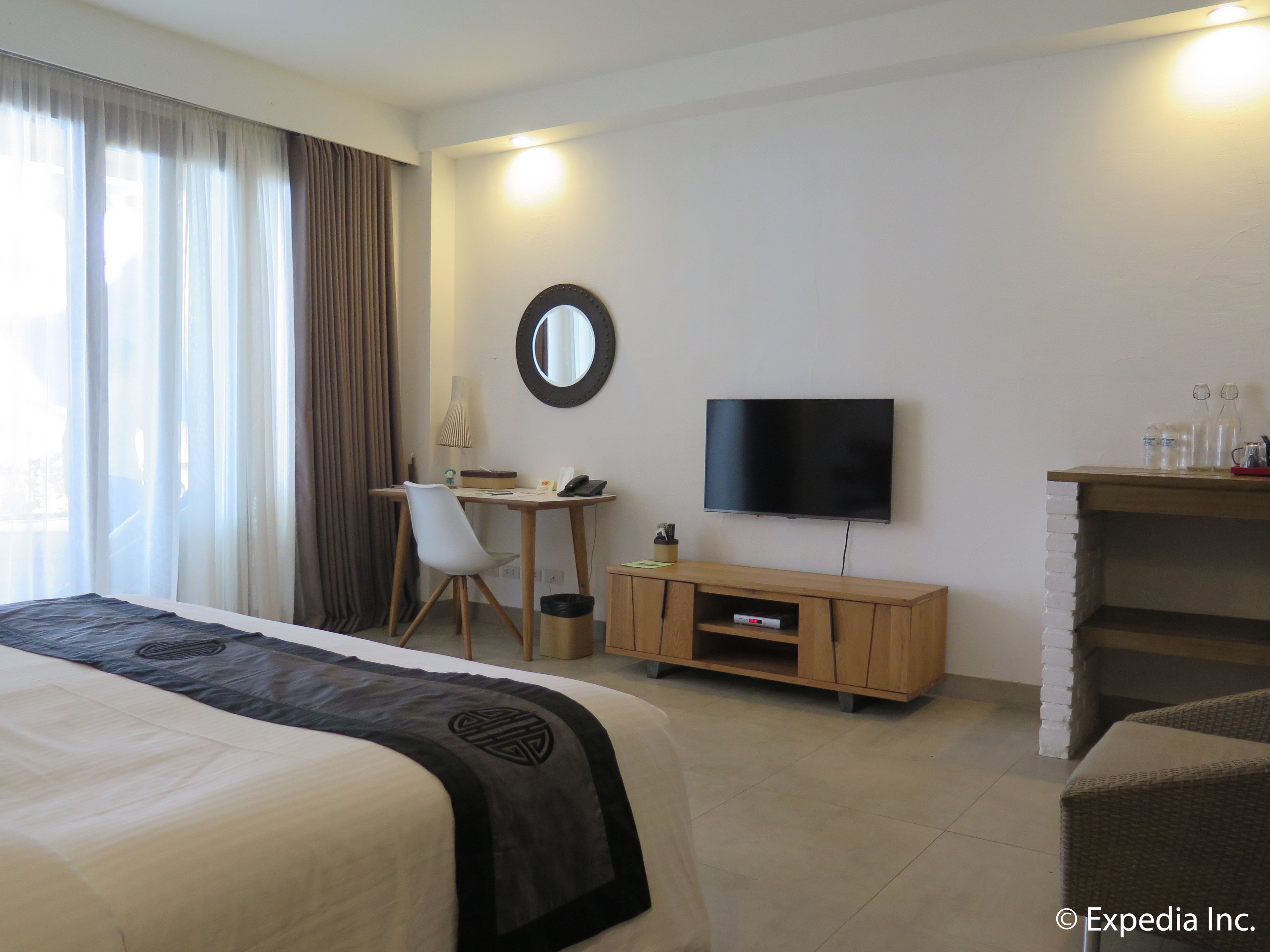 A hotel room with a bed, a desk, a chair, a TV, and a small cabinet.