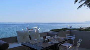 Enjoy a meal with a view of the sea from this outdoor dining area, featuring a table set with placemat, cutlery, and glass, and comfortable seating for two.