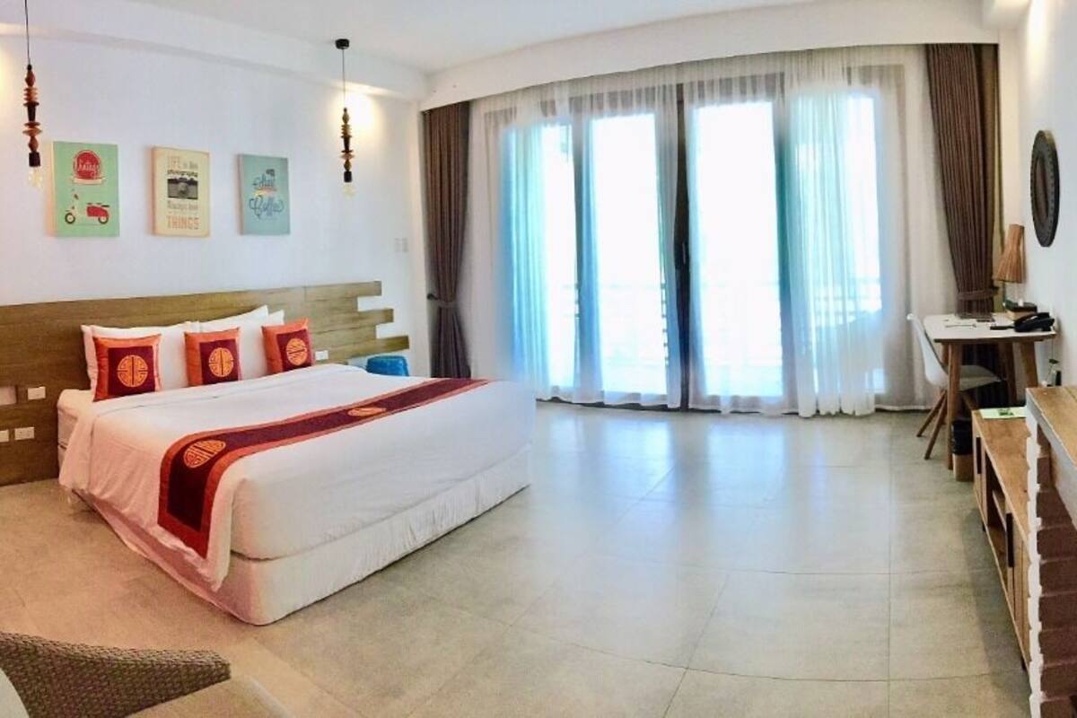 Une chambre d’hôtel équipée d’un lit, d’un bureau, d’une télévision et d’une grande fenêtre avec des rideaux.