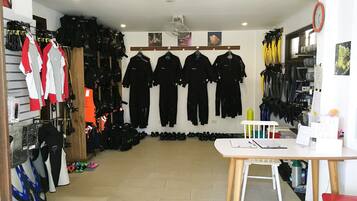 Una habitación con una mesa blanca, una silla roja y una silla blanca. Chaquetas negras y rojas cuelgan en la pared.