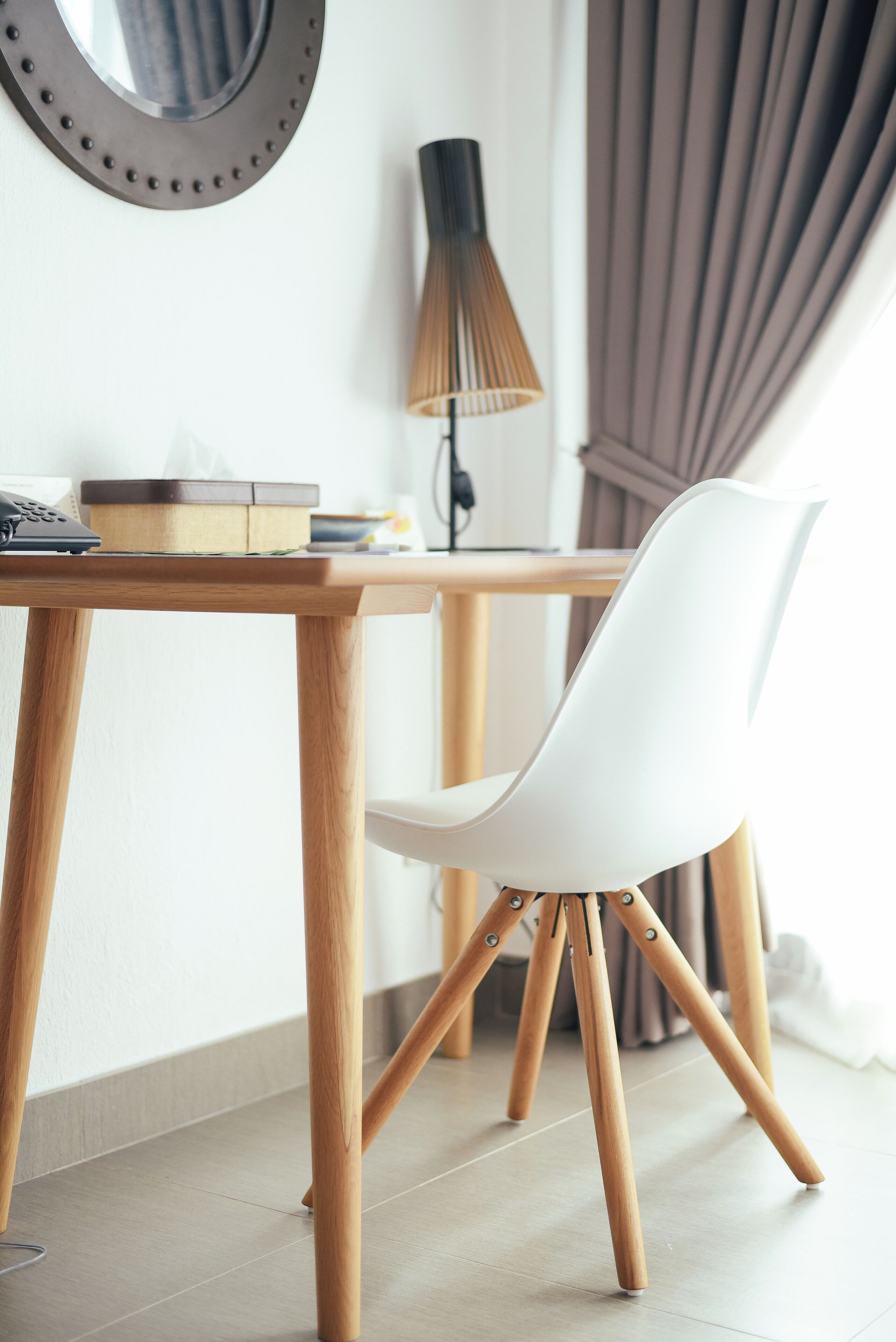 A modern room with a wooden table, a white chair, a lamp, and a mirror on the wall.