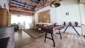 Una habitación espaciosa con mesa de fútbol, vigas de madera y un ventanal grande.