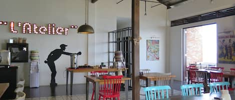 Interior de restaurante con barra, sillas rojas y azules, y un ventilador de techo.