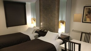 Une chambre d’hôtel avec deux lits simples, une petite table, une chaise, un bureau, un miroir et un téléviseur.