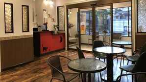 L’intérieur d’un restaurant, avec un comptoir d’accueil, des chaises en osier, des tables rondes et de grandes fenêtres donnant sur la rue.