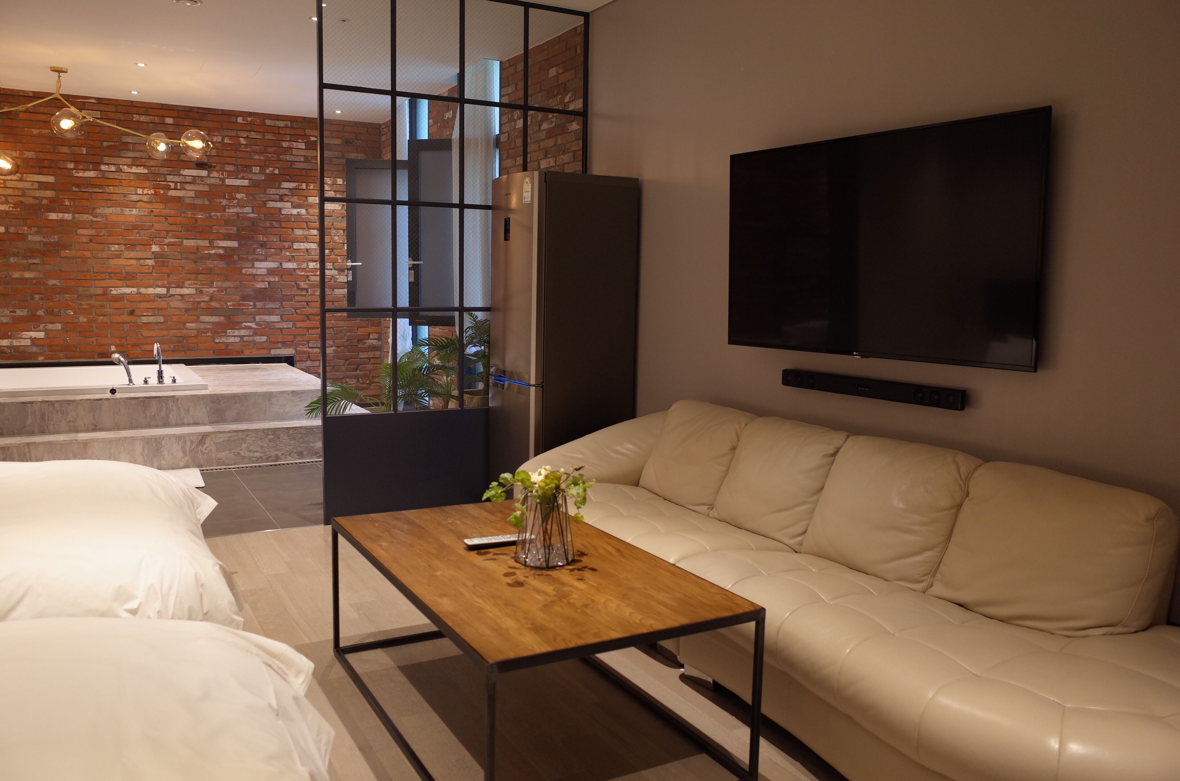 Een moderne woonkamer met een witte leren bank, een houten salontafel met een vaas, een grote flatscreen televisie en een metselwerk muur.