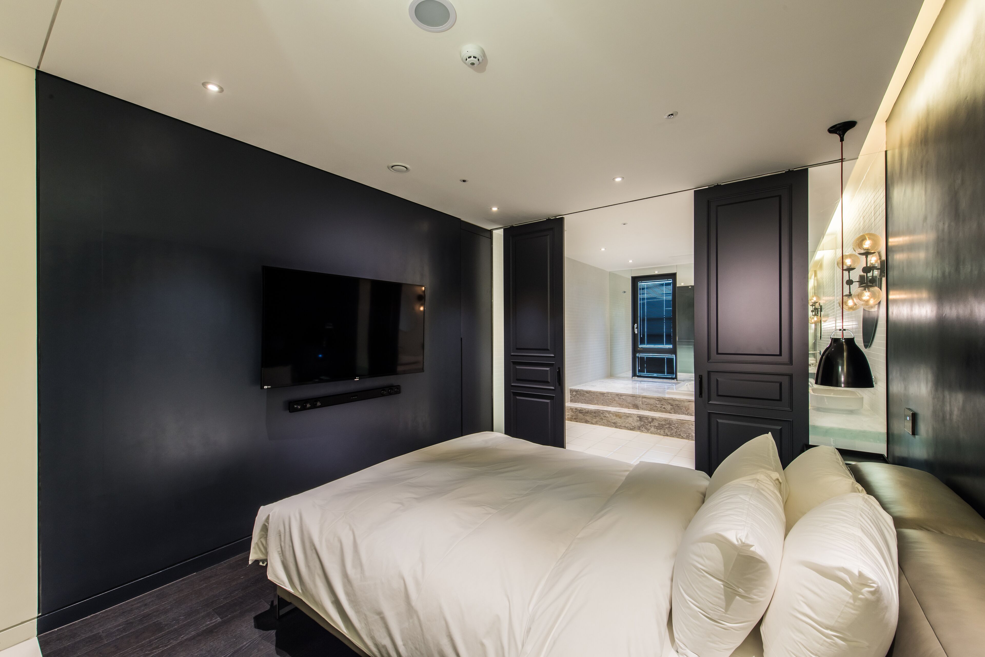 A modern bedroom with a large bed, a flat-screen TV mounted on the wall, and a large mirror reflecting the room.
