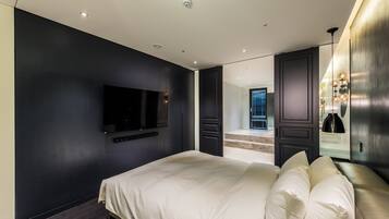 A modern bedroom with a large bed, a flat-screen TV mounted on the wall, and a large mirror reflecting the room.
