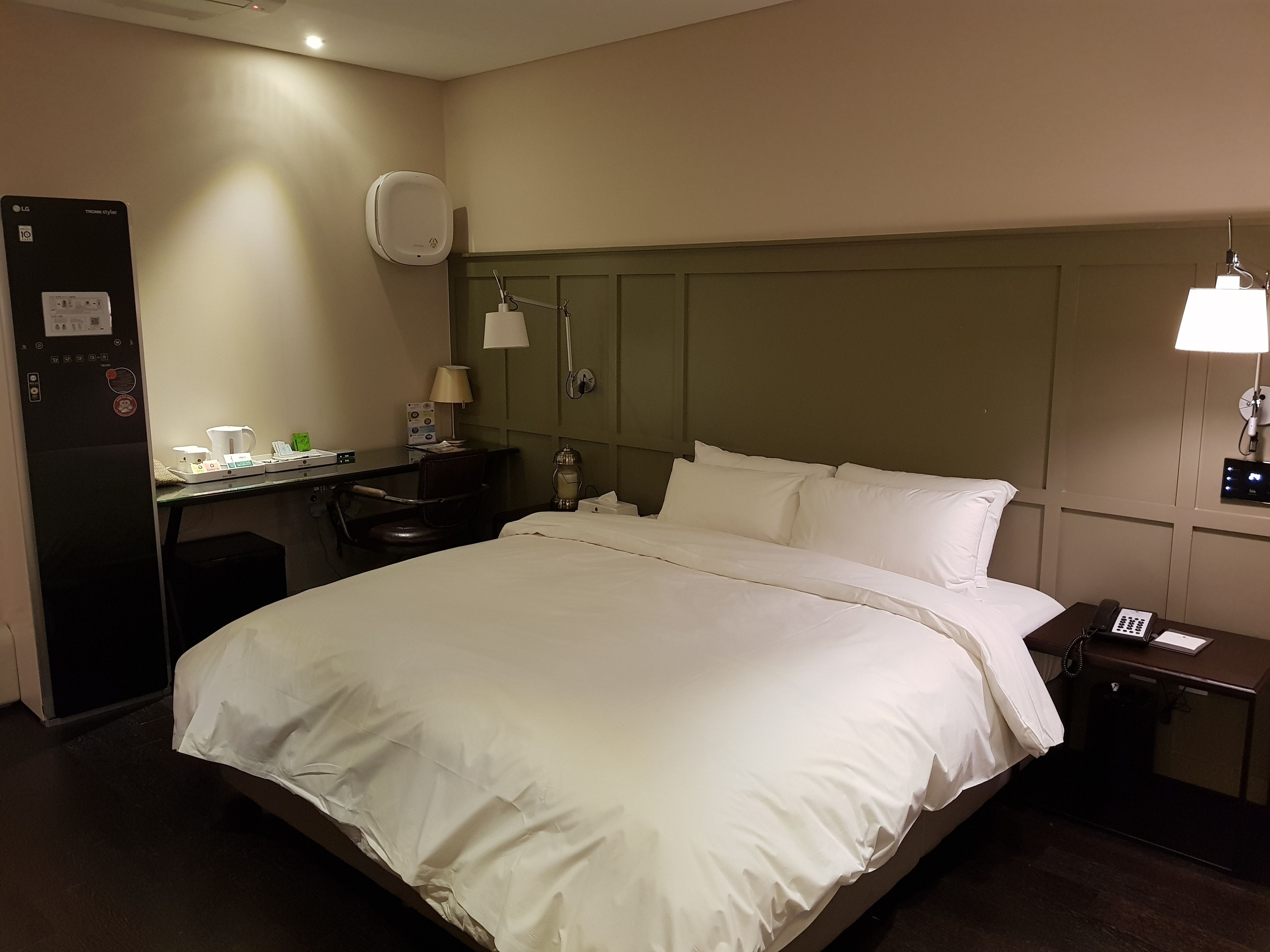 A hotel room with a bed, desk, chair, lamp, and a phone on the nightstand.