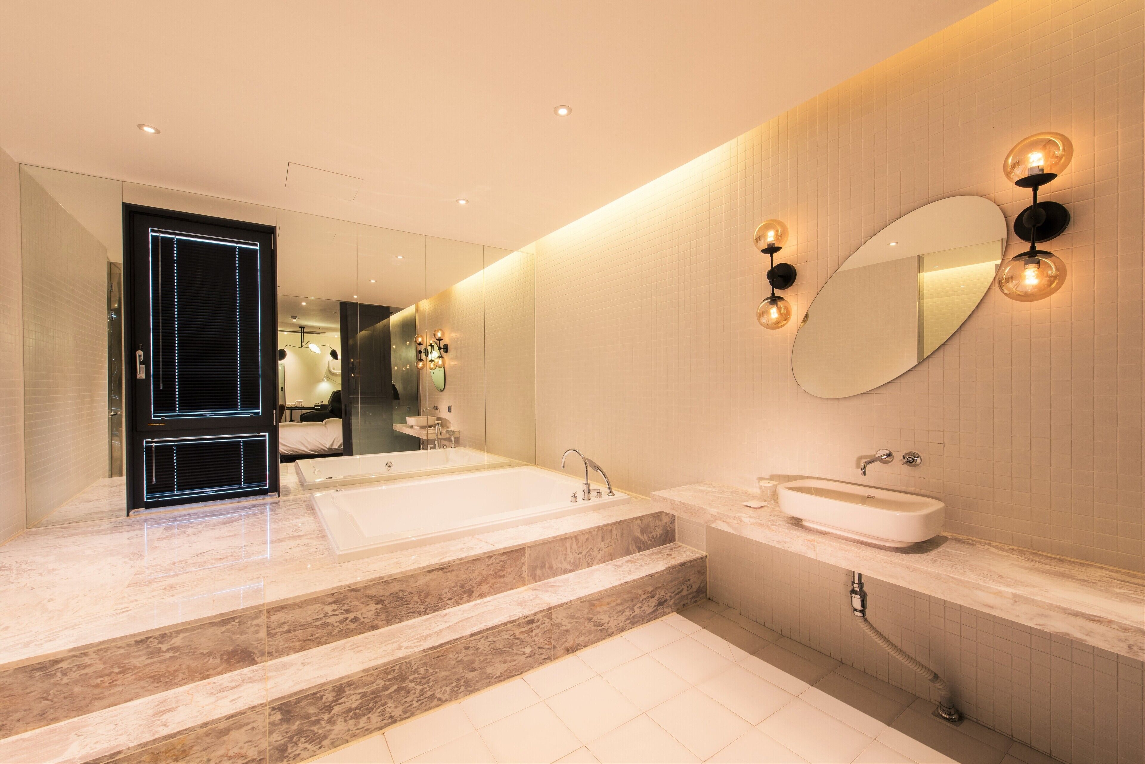 Une salle de bain moderne avec une grande baignoire, un lavabo séparé et un miroir agrémenté de luminaires fixés au mur.