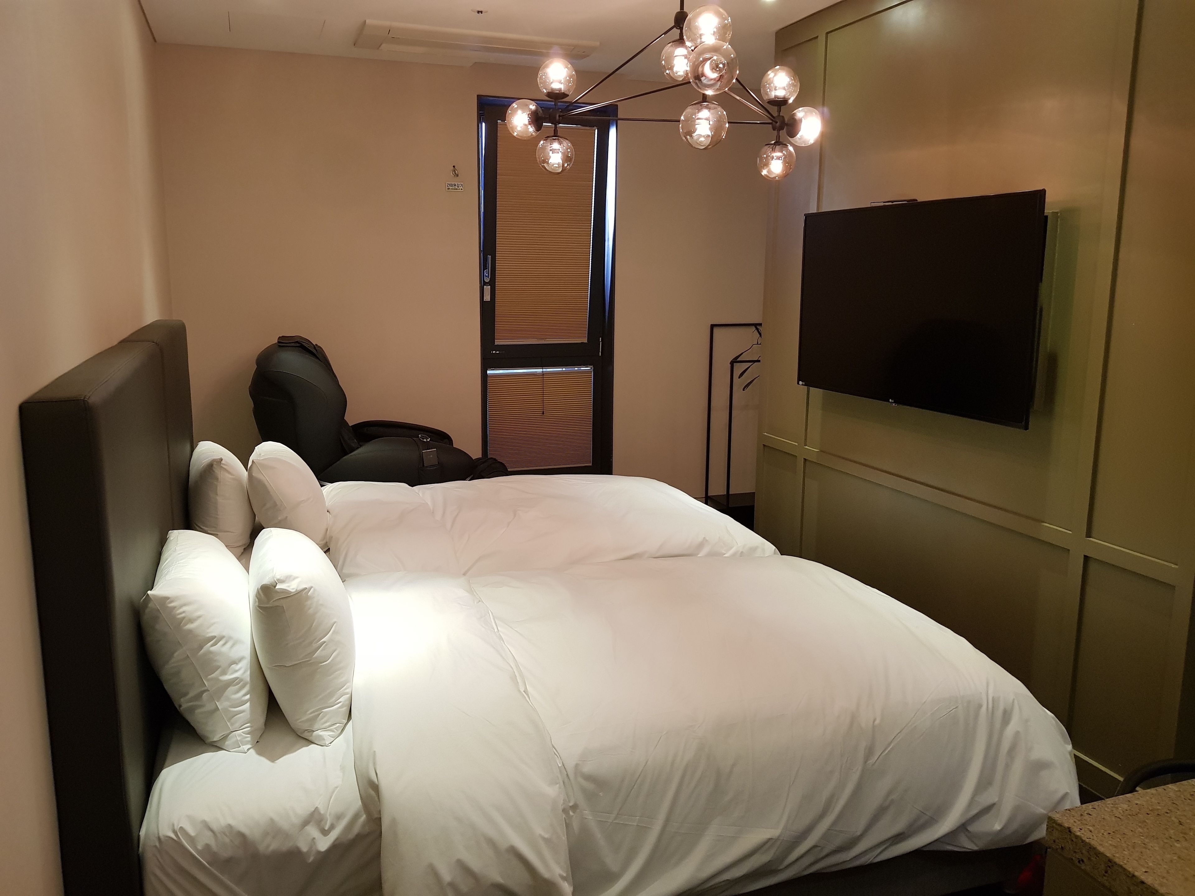 A hotel room with a large bed, a black chair, a television, and a ceiling light fixture.