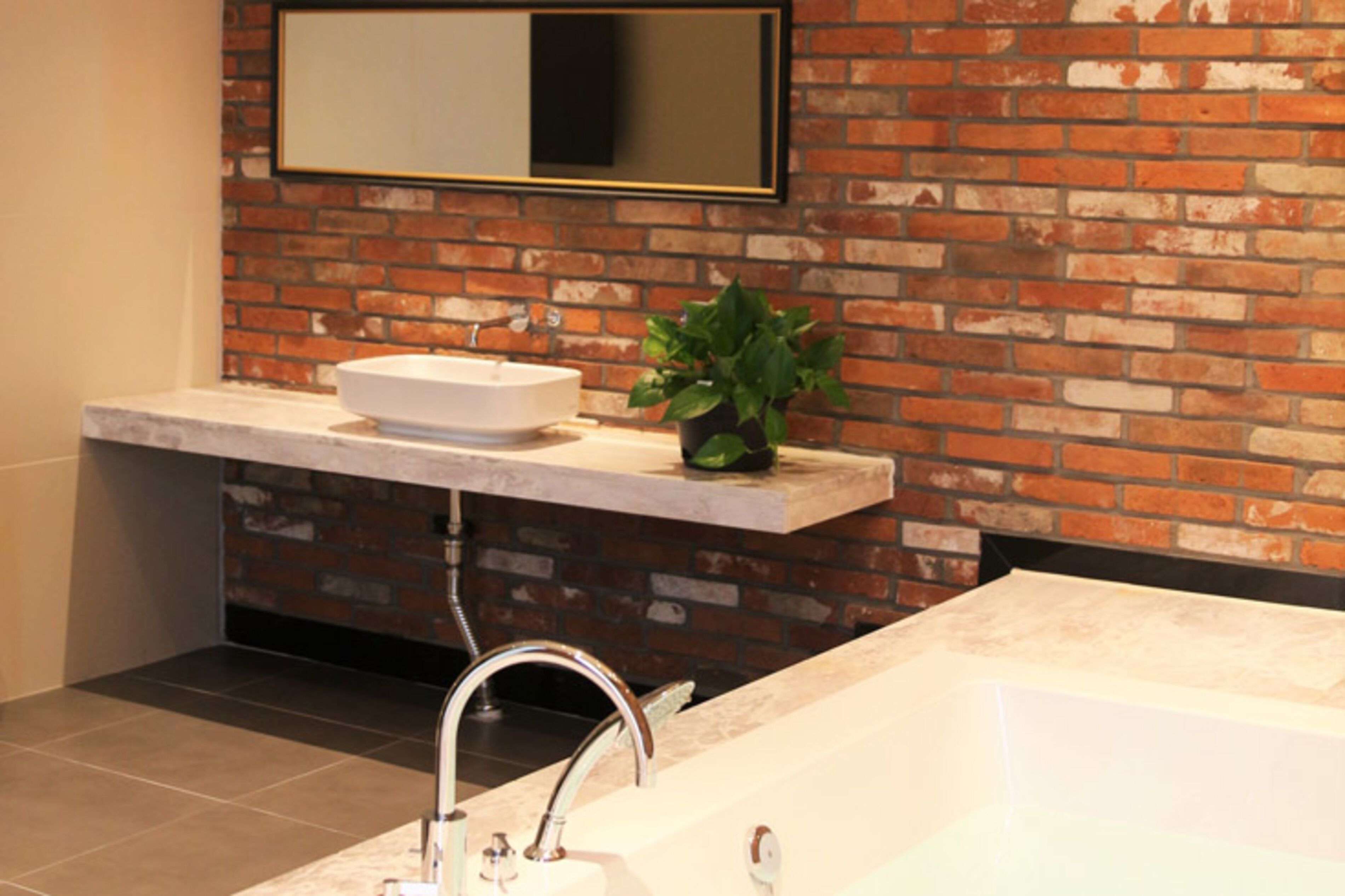 A bathroom with a white sink, a large mirror, and a brick wall.