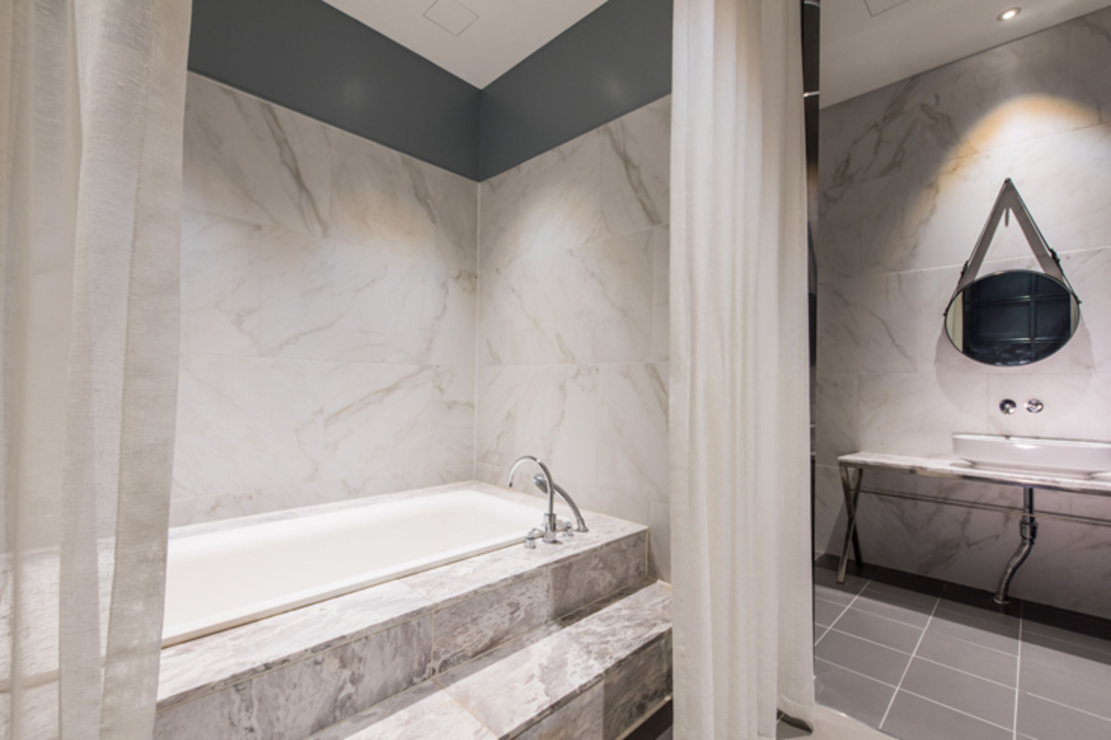A modern bathroom with a marble sink, a bathtub, and a mirror.