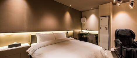 Una habitación de hotel moderna con una cama grande, mesitas de noche, un escritorio con silla, un sillón de masaje y un minibar.