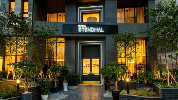 A hotel entrance with a sign reading "HOTEL STENDHAL," surrounded by potted plants and a brick pathway. - Hotel Stendhal (Daejeon)