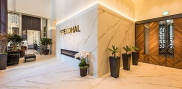 A hotel lobby with a marble floor, a reception desk, and potted plants.