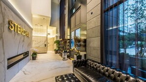 A modern hotel lobby with a black leather sofa, a reception desk, and a large window offering a view of the outdoors. - Hotel Stendhal (Daejeon)