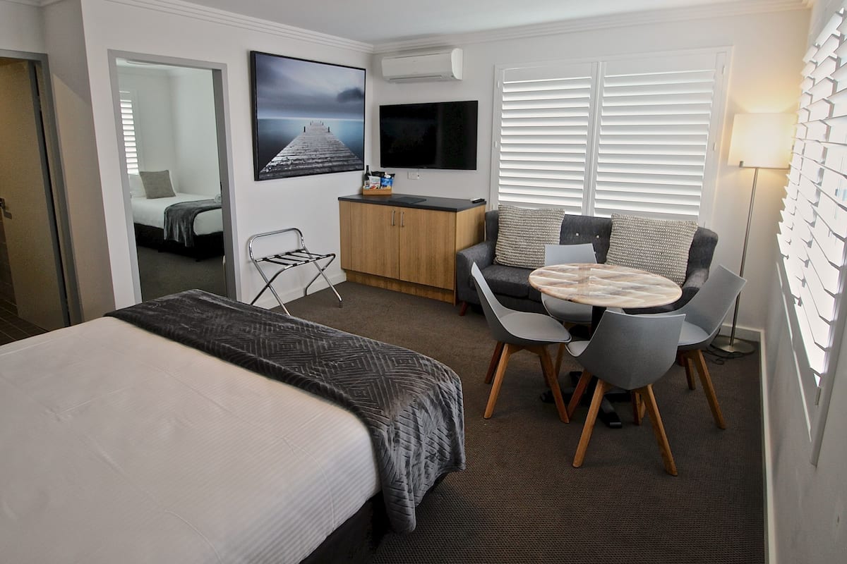 A hotel room with a bed, a desk, a chair, a sofa, a TV, and a window with blinds.