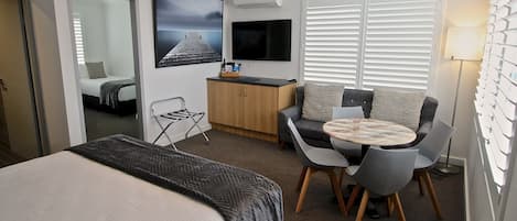 A hotel room with a bed, a desk, a chair, a sofa, a TV, and a window with blinds.
