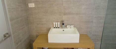 A bathroom with a white sink, wooden vanity, and a small window.