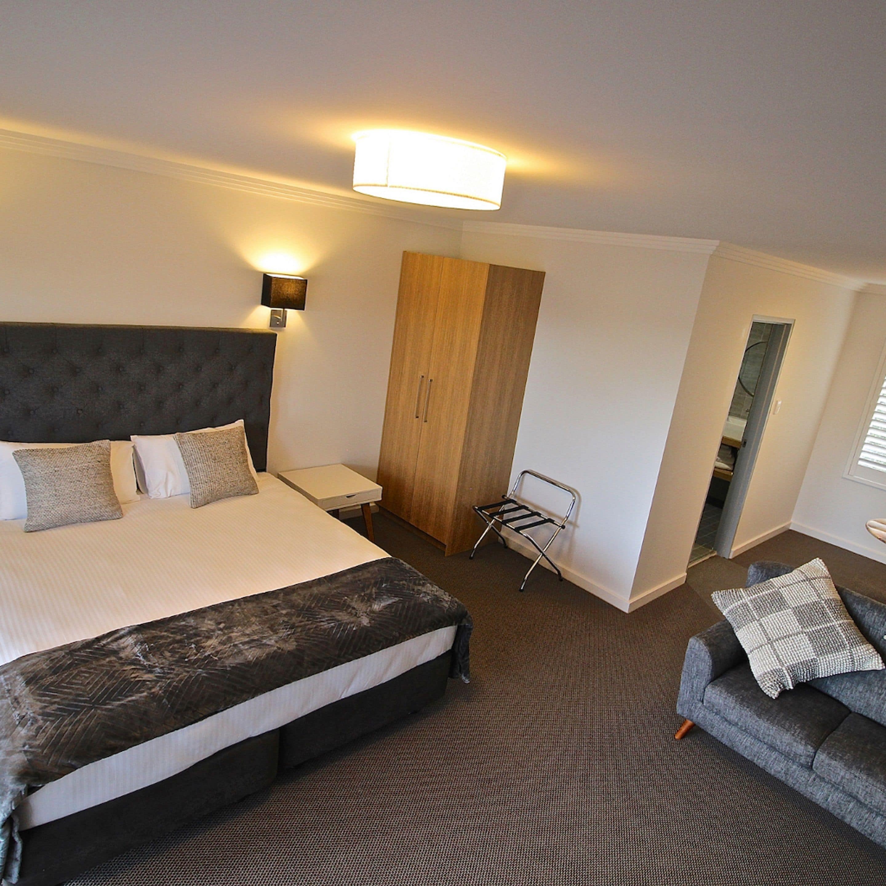 Une chambre d’hôtel avec un grand lit, une table de chevet, une armoire en bois, une chaise et un canapé.