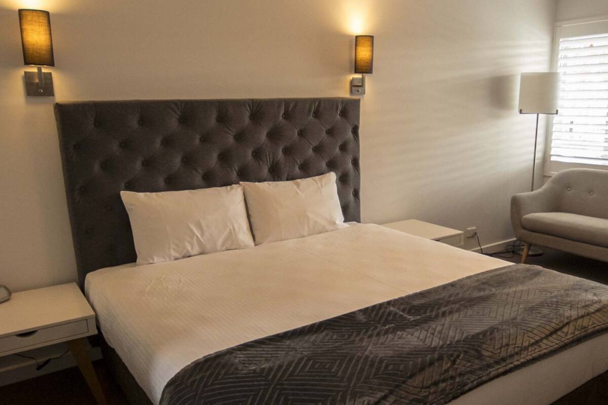 A neatly made bed with a tufted headboard, two bedside tables, a chair, and a lamp.