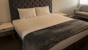 A neatly made bed with a tufted headboard, two bedside tables, a chair, and a lamp.