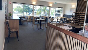 A modern cafe with wooden furniture, large windows, and a view of the outdoors. - Quays Hotel (Batemans Bay)
