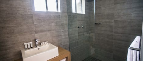 Ein modernes Badezimmer mit einer gläsernen Duschkabine, einem Holzwaschtisch und einem Fenster über dem Spiegel.