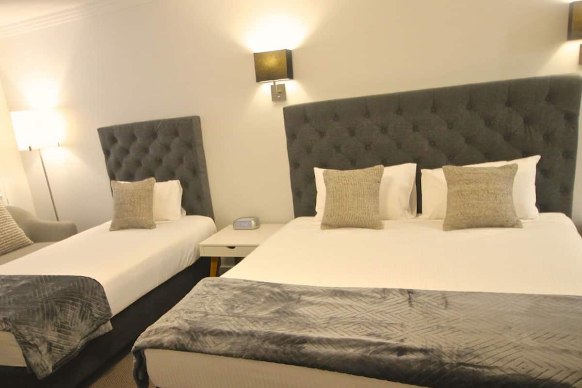 A hotel room with two beds, each with a tufted headboard, a bedside table, and a lamp.