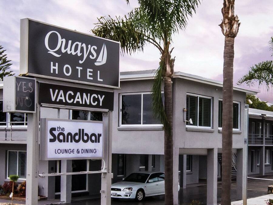Señal de hotel que indica Quays Hotel, con un anuncio de disponibilidad y un letrero de Sandbar Lounge & Dining.