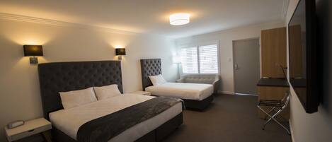 A hotel room with two beds, a bedside table, a lamp, a TV, and a wardrobe.