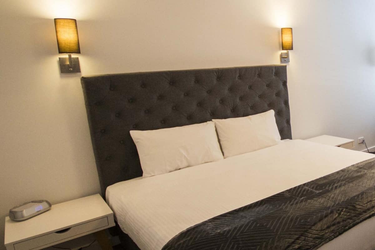 A hotel room with a tufted headboard, a white bedspread, and two wall-mounted lamps.