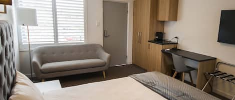 A hotel room with a large bed, a sofa, a desk, and a TV.