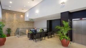Un espace d’accueil comprenant un comptoir de réception, une réceptionniste, un panneau d’identification de la réception, un escalier et des plantes en pot.