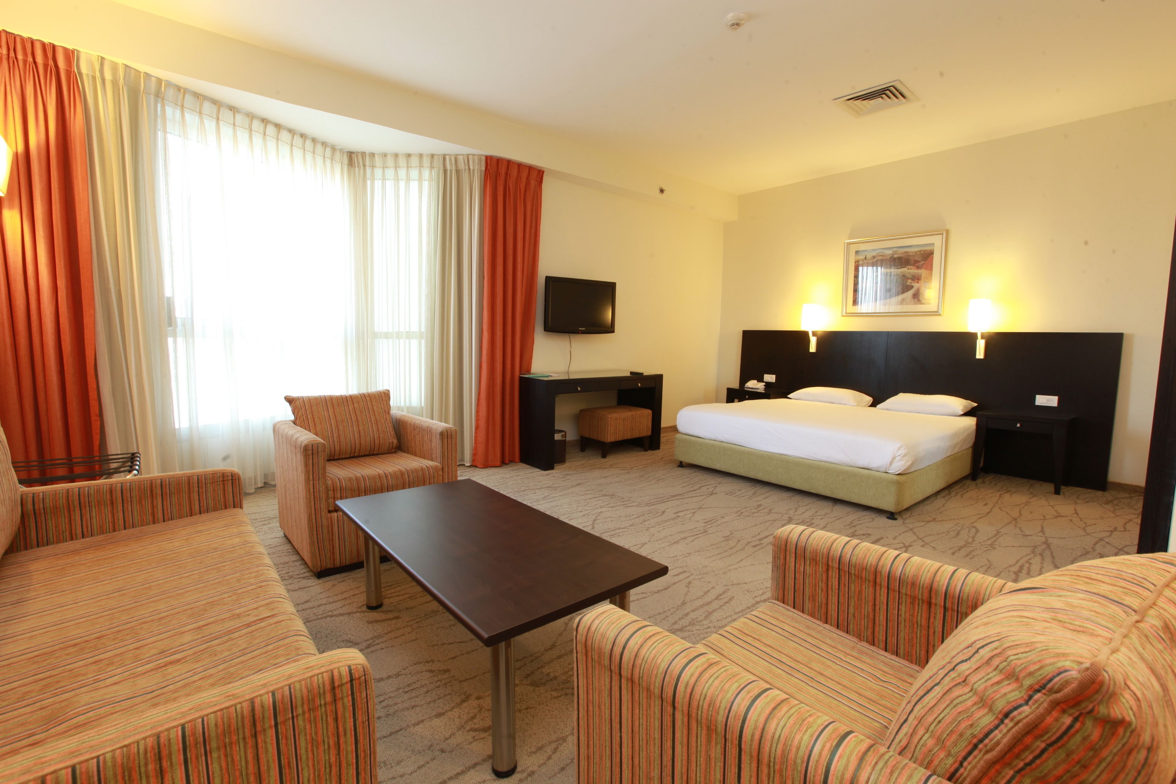 Une chambre d’hôtel comprenant un lit, deux fauteuils, un canapé, une télévision et un bureau.