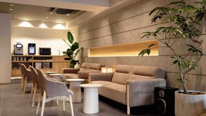 A modern lounge area with a sofa, chairs, a coffee machine, a TV, and a large potted plant. - HOTEL PAUL HOUSE (Tokyo)
