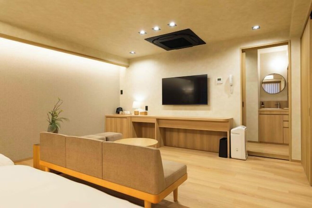 Een moderne hotelkamer met een bed, een zithoek, een aan de muur bevestigde televisie en een kleine kitchenette.