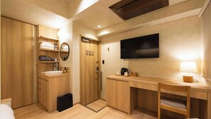 A hotel room with a wooden wardrobe, a desk with a flat-screen TV, a bedside table with a lamp, and a small trash bin. - HOTEL PAUL HOUSE (Tokyo)