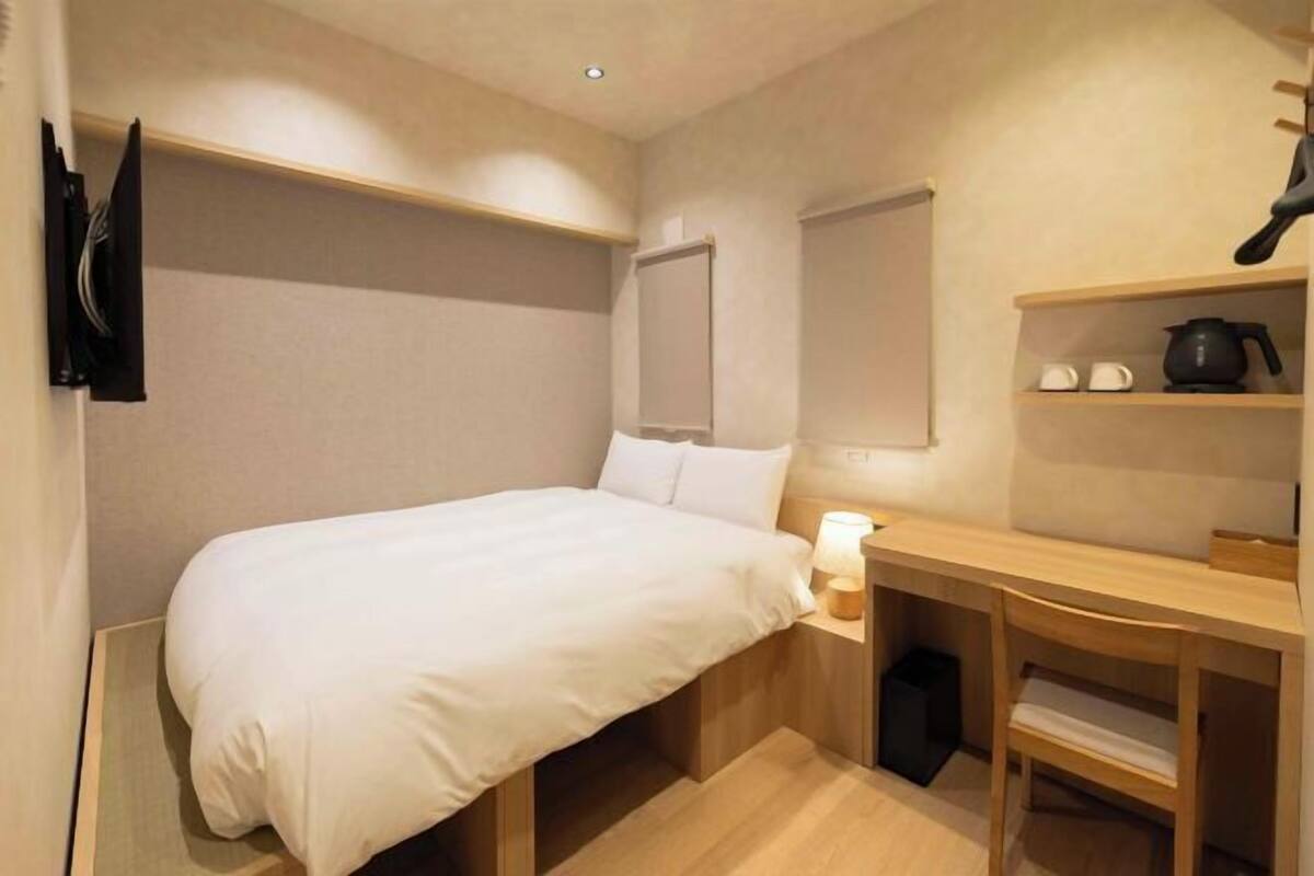 A compact hotel room with a bed, bedside table, and a small desk with a chair.