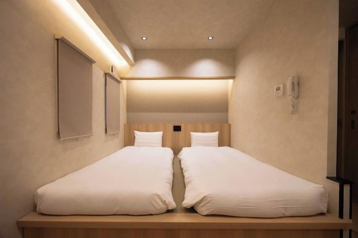 A small, cozy room with two single beds, a wooden headboard, and a wall-mounted phone.
