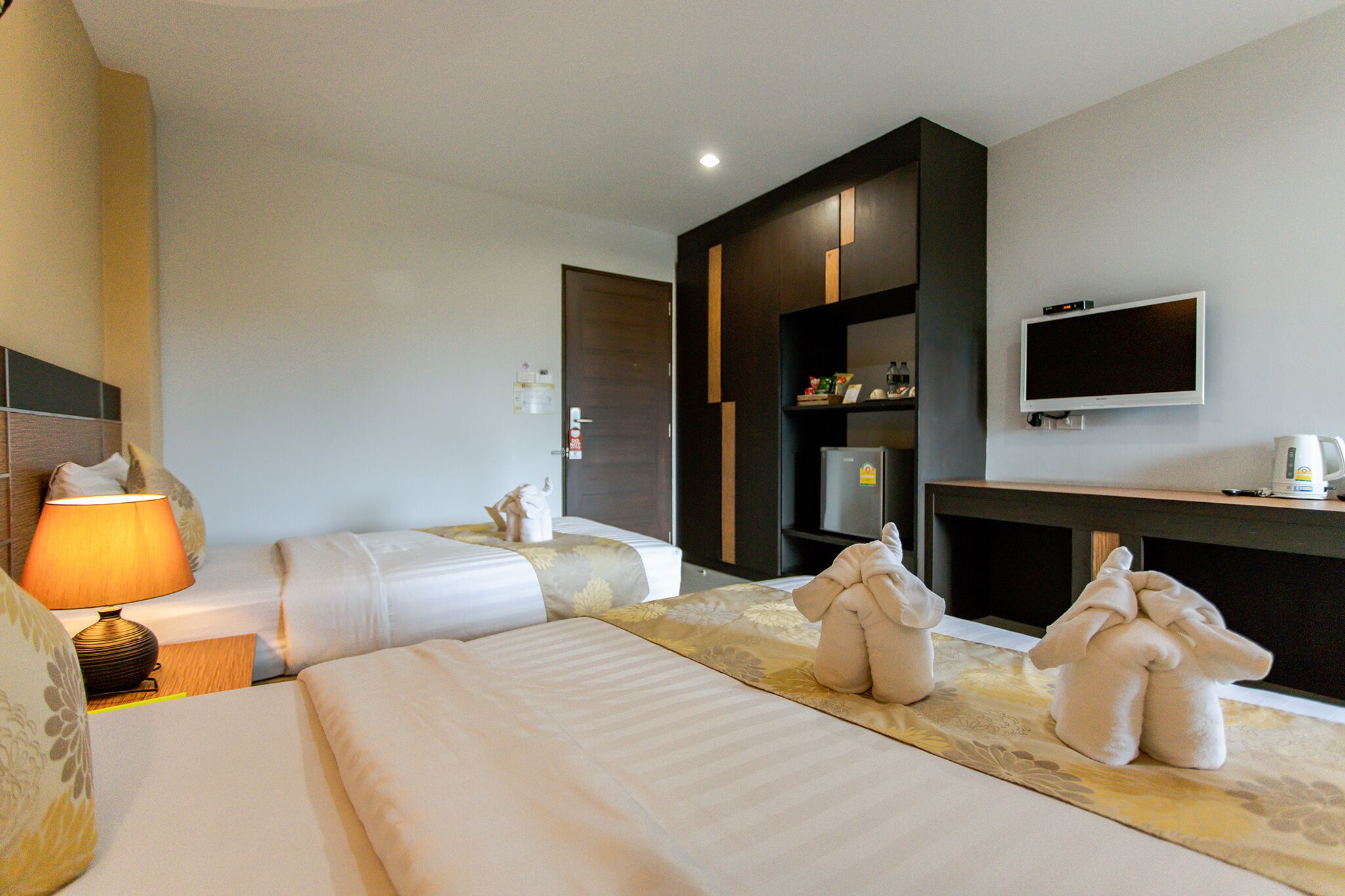 A hotel room with two beds, a TV, a minibar, and a lamp.