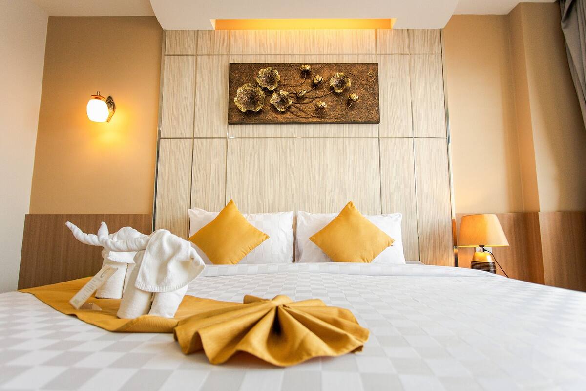 Habitación de hotel con una cama grande, ropa de cama blanca, un adorno de pared, una lámpara de pared y una lámpara de noche.