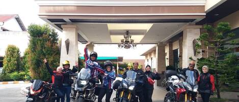 A group of people with motorcycles in front of a building with a sign that reads "TISANISULINAS".