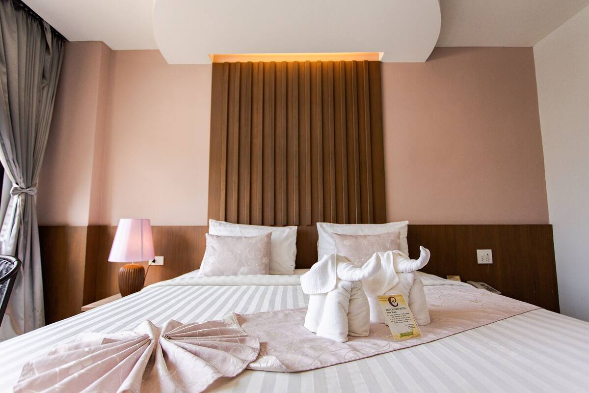 Una habitación de hotel con cama, almohadas, lámpara, toalla y un cartel.